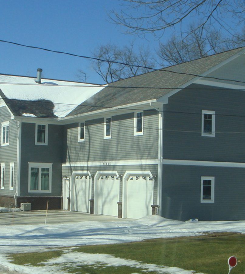 Gray house with snow-covered yard and driveway.