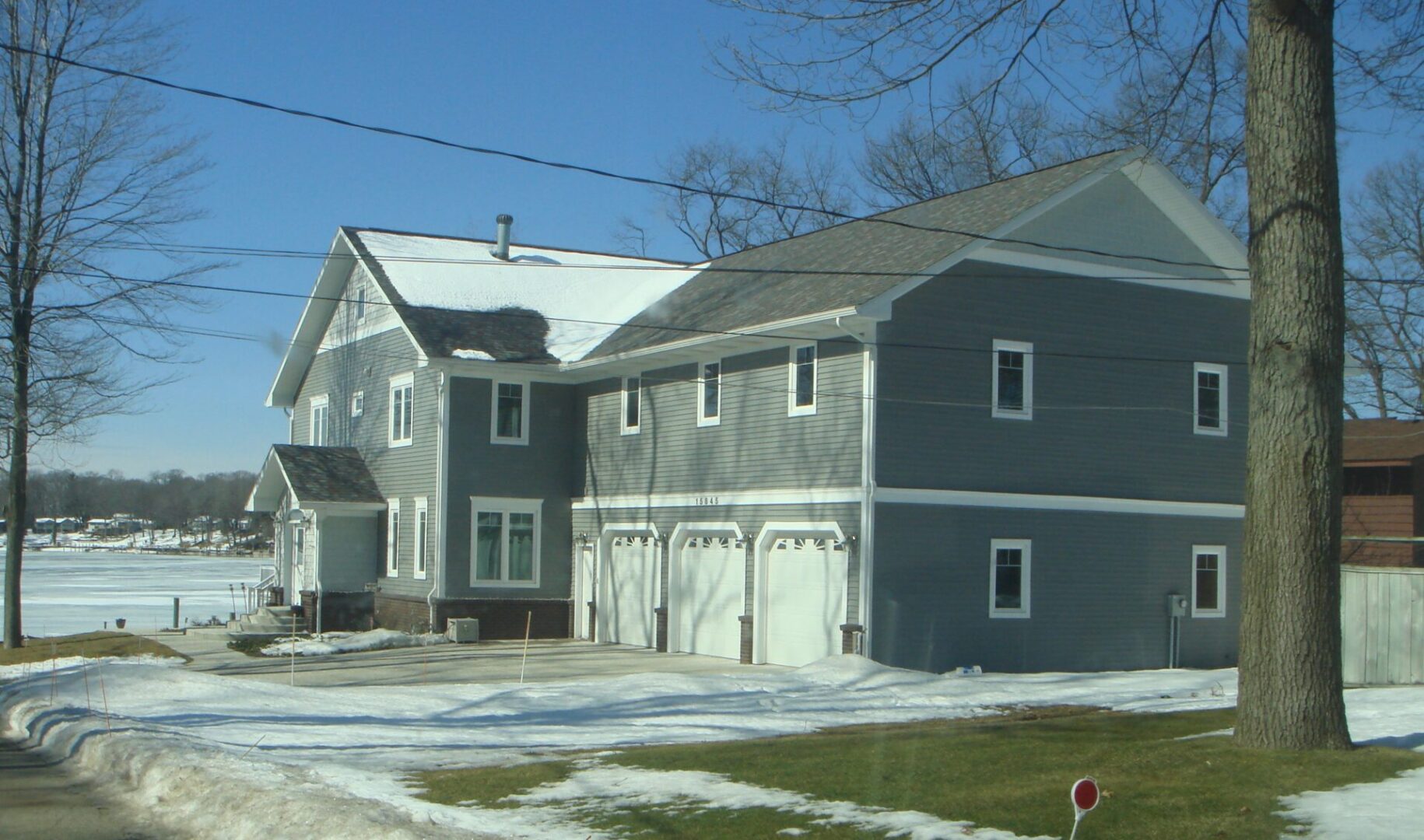 Large house with snow-covered yard and trees.
